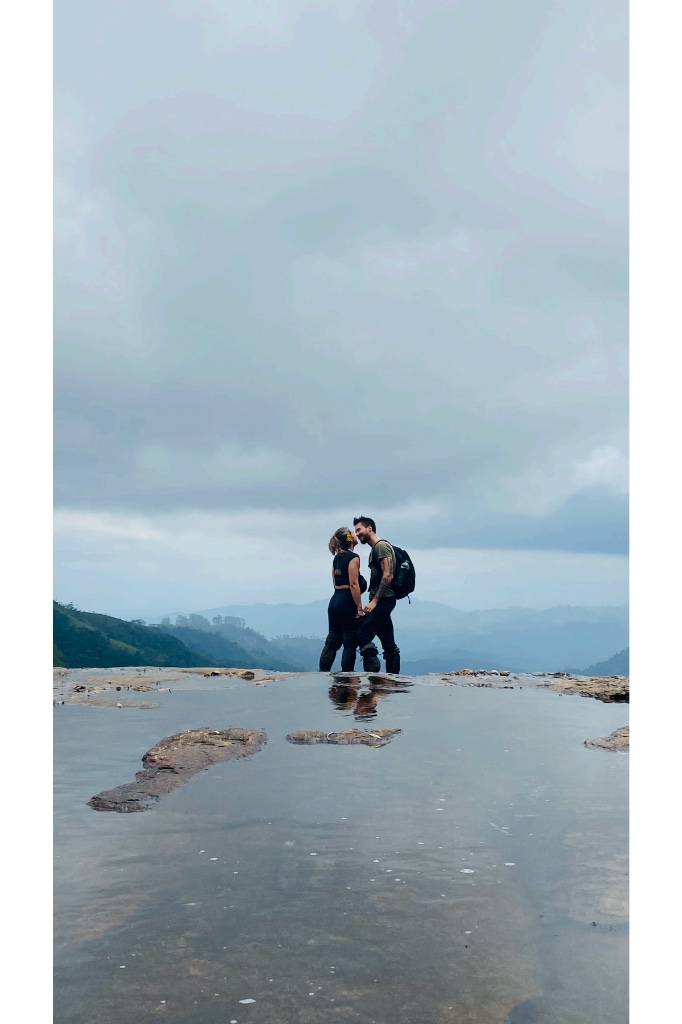 Couple embracing on a mountain rock summit plateau reflecting in a shallow pool of water overlooking misty Knuckles peaks
