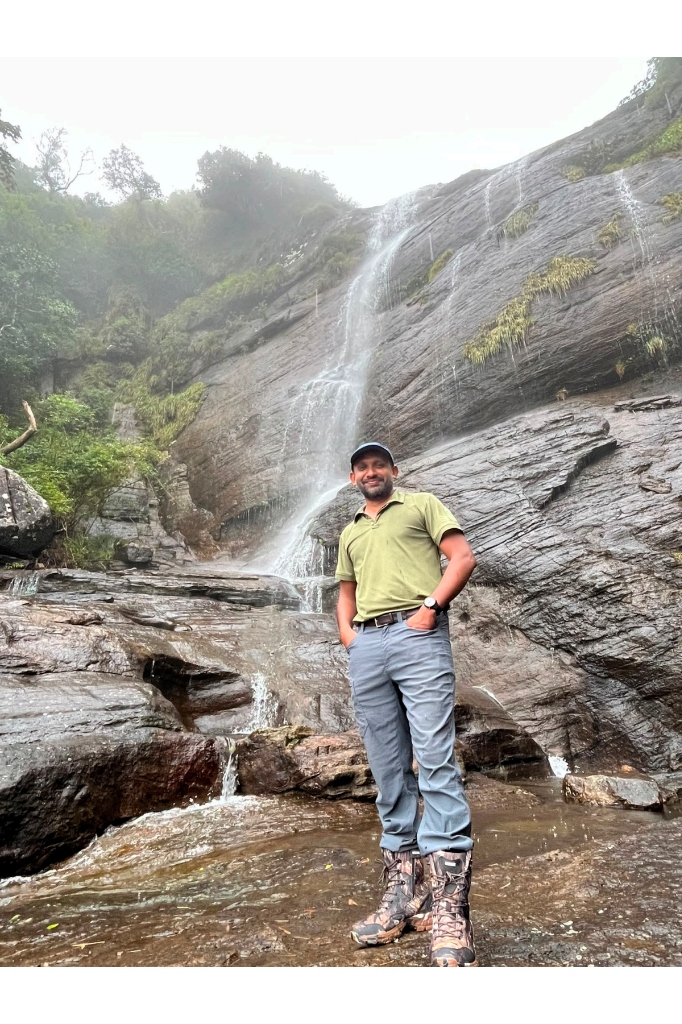 Local trekking guide Ravi smiling in front of a cascading mountain waterfall in the Knuckles Range