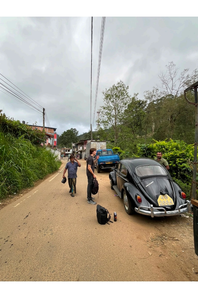 Traveler and guide Ravi beside a classic vintage Volkswagen Beetle on a rural Sri Lankan mountain road