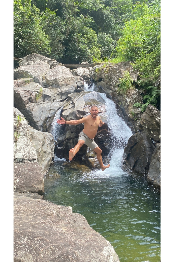 Adventure traveler jumping and leaping mid-air into a deep natural rock pool beneath a cascading Knuckles jungle waterfall