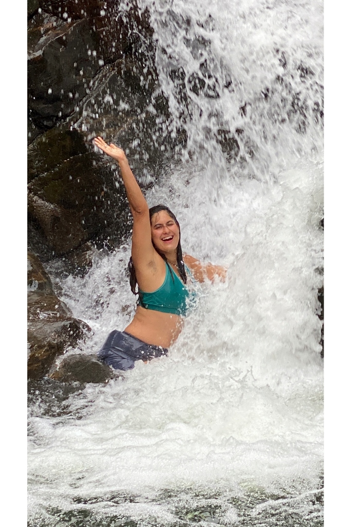 Joyful swimmer celebrating with arm raised under a rushing cascade shower in a natural Knuckles waterfall pool